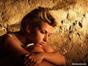 woman sitting looking sad with sun shining on the rock wall behind her