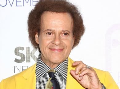 Richard Simmons in a yellow suit smiles for the camera