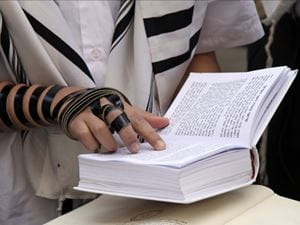 Tefillin clad hand reading from a Siddur