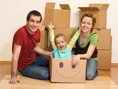 A mother and father packing for a move, with a smiling child in a box.