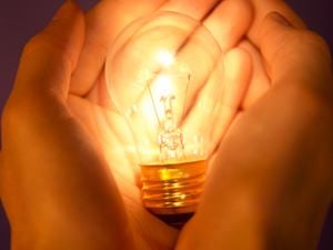 Two hands cupping lit lightbulb