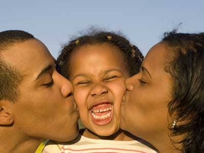 African-American parents kissing daughter